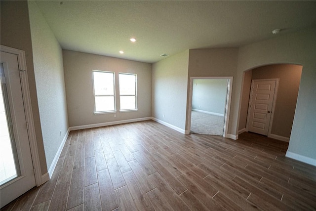 empty room with dark wood-style floors, baseboards, and arched walkways