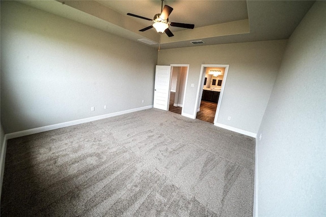 unfurnished bedroom with ceiling fan, connected bathroom, carpet flooring, baseboards, and a raised ceiling