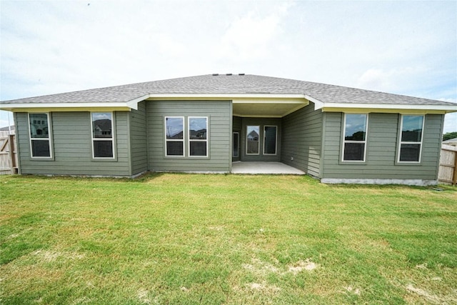 rear view of house featuring roof with shingles, a lawn, a patio area, and fence