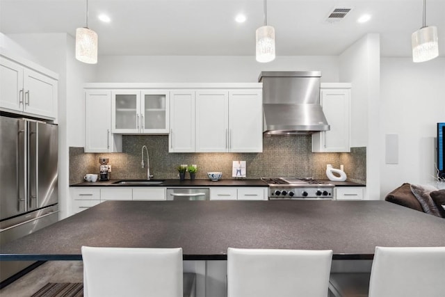 kitchen featuring decorative light fixtures, wall chimney exhaust hood, dark countertops, and glass insert cabinets