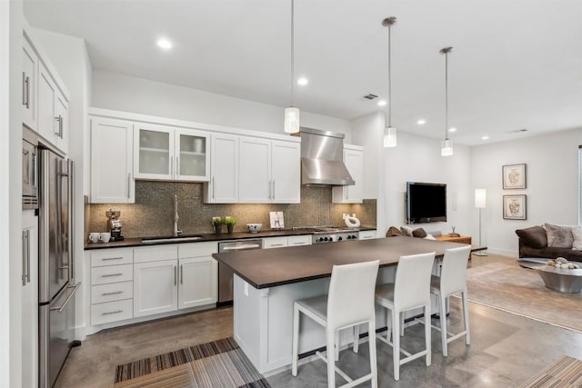 kitchen featuring appliances with stainless steel finishes, pendant lighting, sink, white cabinets, and wall chimney exhaust hood