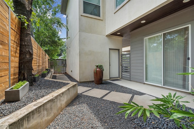 property entrance with fence, stucco siding, and a patio area