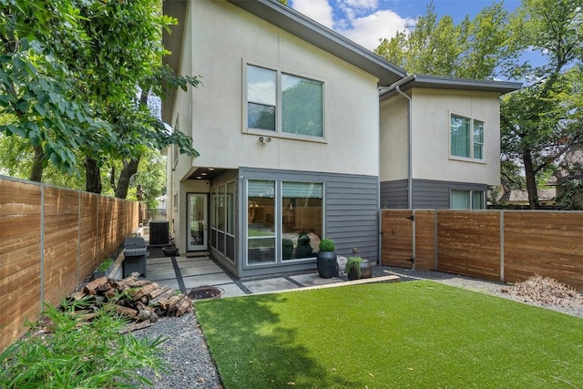 rear view of property with stucco siding, a lawn, a fenced backyard, and cooling unit