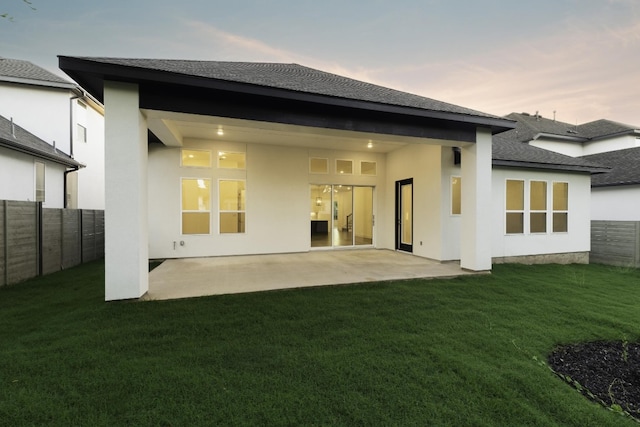 back house at dusk featuring a yard and a patio area