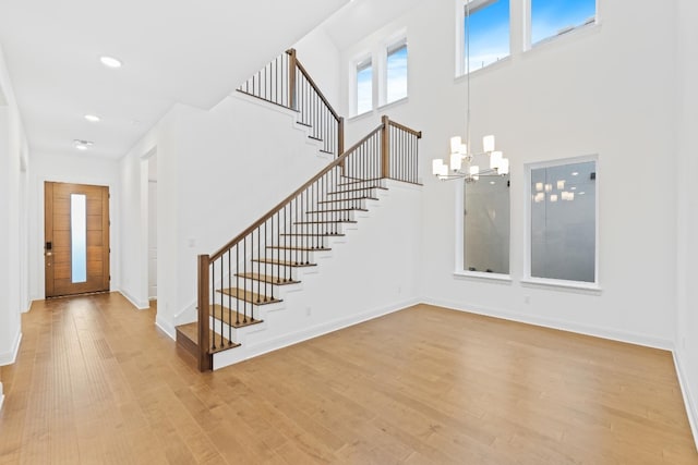 entrance foyer with light wood-type flooring, a towering ceiling, and a chandelier