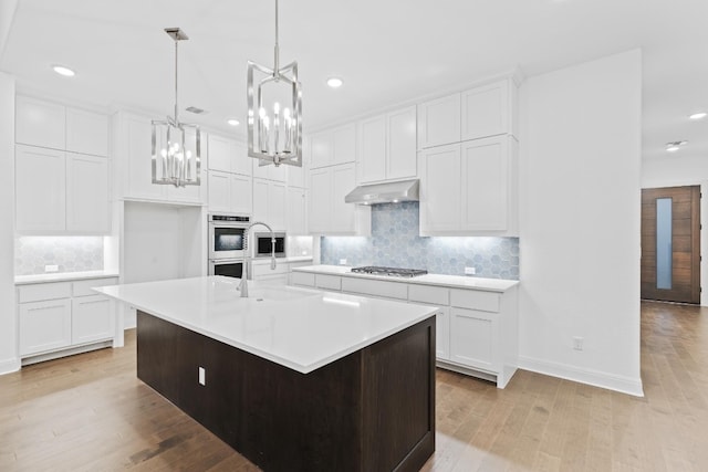 kitchen with white cabinets, an island with sink, and light hardwood / wood-style flooring