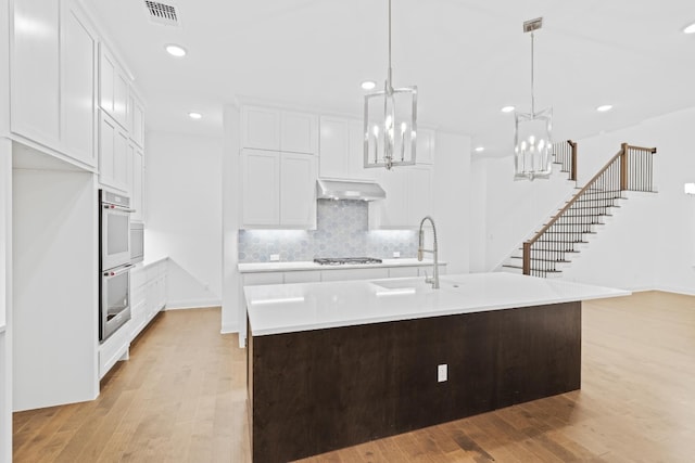 kitchen with decorative light fixtures, sink, an island with sink, and light hardwood / wood-style flooring