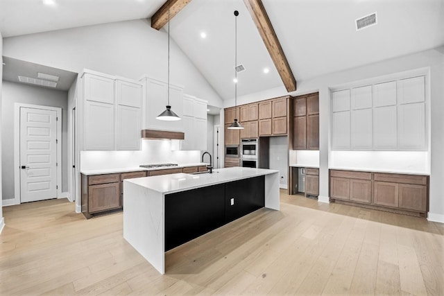 kitchen with light hardwood / wood-style floors, a large island with sink, beam ceiling, and pendant lighting