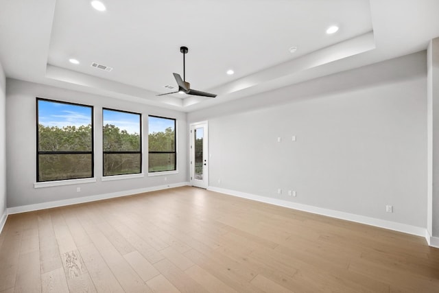 unfurnished room with light hardwood / wood-style flooring, ceiling fan, and a raised ceiling