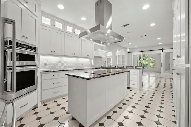 kitchen with island range hood, a kitchen island, kitchen peninsula, a barn door, and white cabinetry