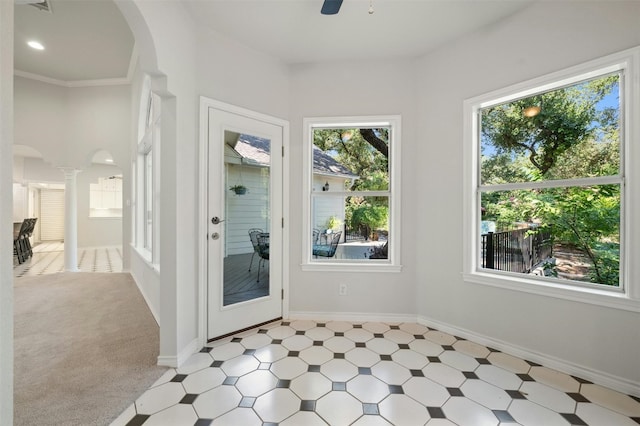 doorway featuring ceiling fan, decorative columns, ornamental molding, and light colored carpet