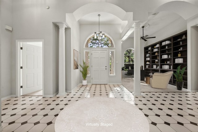 entrance foyer with light tile patterned floors, ornate columns, a high ceiling, and ceiling fan with notable chandelier