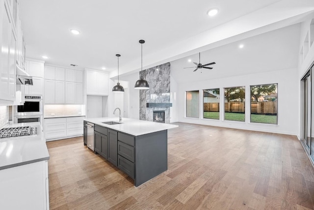 kitchen featuring a kitchen island with sink, white cabinets, hanging light fixtures, light hardwood / wood-style flooring, and vaulted ceiling with beams