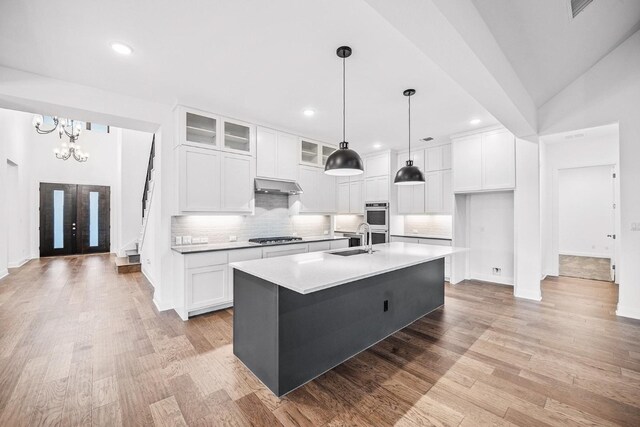 kitchen with exhaust hood, a center island with sink, light hardwood / wood-style flooring, white cabinetry, and stainless steel appliances