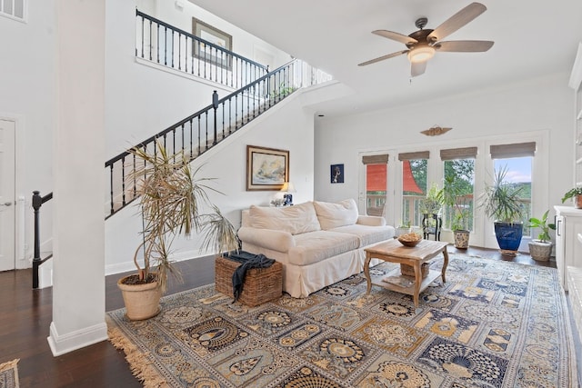 living room with dark wood-type flooring, ceiling fan, and a towering ceiling