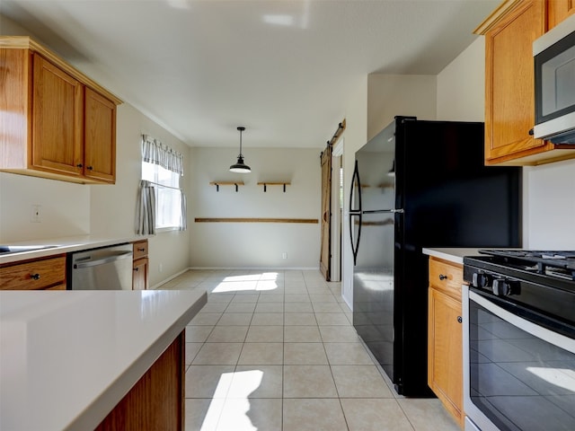 kitchen with appliances with stainless steel finishes, a barn door, light tile patterned flooring, and hanging light fixtures