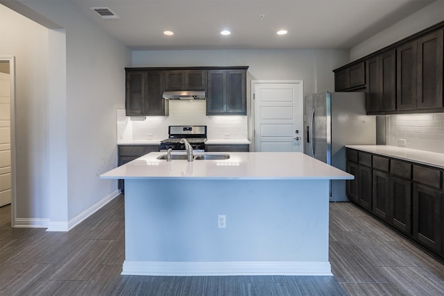 kitchen featuring appliances with stainless steel finishes, an island with sink, dark brown cabinetry, sink, and backsplash