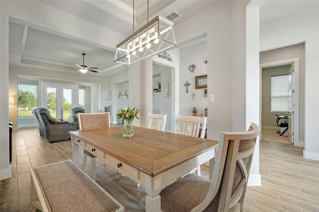 dining room featuring light wood-type flooring, ceiling fan with notable chandelier, french doors, and a raised ceiling