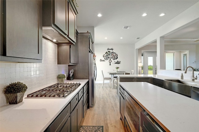 kitchen featuring tasteful backsplash, light wood-type flooring, wall chimney exhaust hood, appliances with stainless steel finishes, and sink