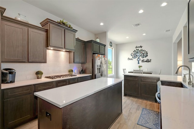 kitchen featuring stainless steel appliances, sink, backsplash, dark brown cabinetry, and light wood-type flooring