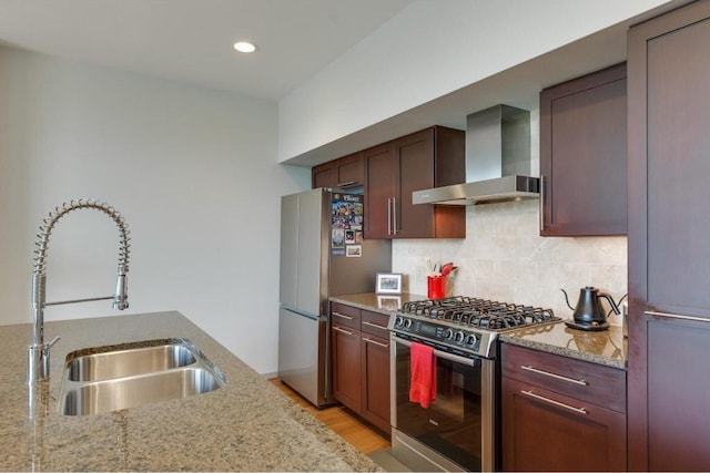 kitchen with wall chimney range hood, sink, appliances with stainless steel finishes, backsplash, and light stone countertops