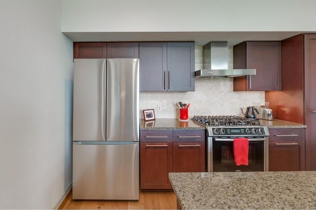 kitchen featuring stainless steel appliances, tasteful backsplash, light stone countertops, wall chimney exhaust hood, and light wood-type flooring