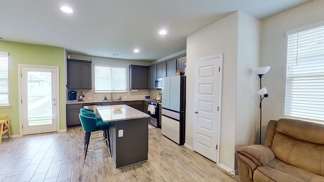 kitchen with stainless steel appliances, a breakfast bar, a kitchen island, sink, and light hardwood / wood-style flooring