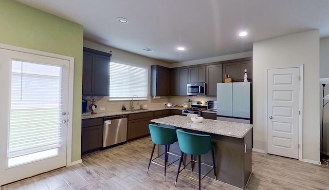 kitchen with stainless steel appliances, sink, a kitchen bar, light stone countertops, and a kitchen island