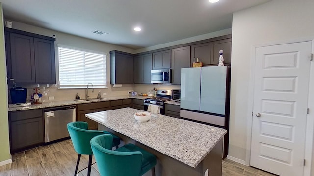 kitchen with sink, a center island, light stone counters, a kitchen bar, and appliances with stainless steel finishes