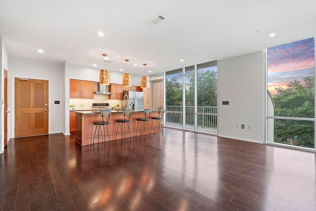 kitchen with stainless steel refrigerator with ice dispenser, decorative light fixtures, a kitchen island with sink, a wall of windows, and a breakfast bar area