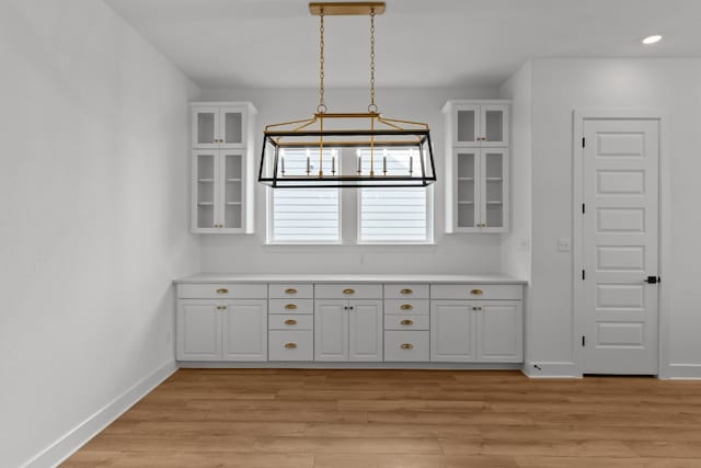 interior space featuring pendant lighting, light wood-type flooring, white cabinetry, and a notable chandelier