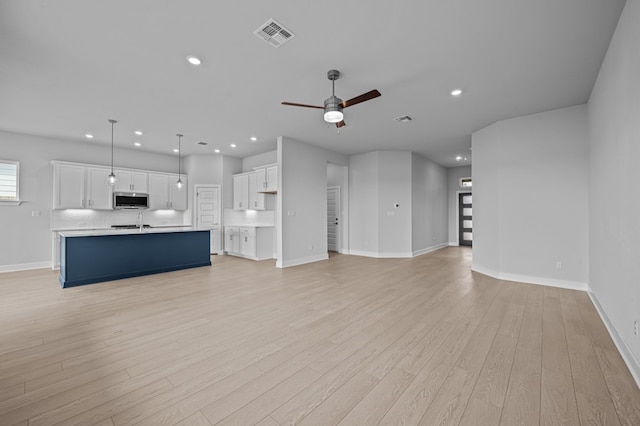 unfurnished living room featuring ceiling fan, light wood-type flooring, and sink