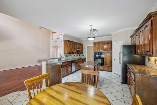 kitchen with dark stone counters, black appliances, light wood-type flooring, a kitchen island, and backsplash