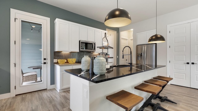 kitchen with decorative light fixtures, white cabinetry, stainless steel appliances, a kitchen breakfast bar, and a kitchen island with sink