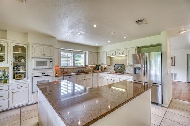 kitchen with a center island, dark stone counters, white appliances, and white cabinets