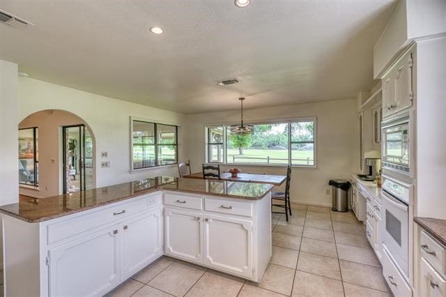 kitchen featuring white oven, stainless steel microwave, light tile patterned floors, kitchen peninsula, and pendant lighting