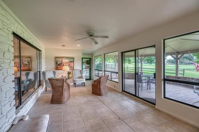 unfurnished sunroom featuring ceiling fan, a fireplace, and plenty of natural light