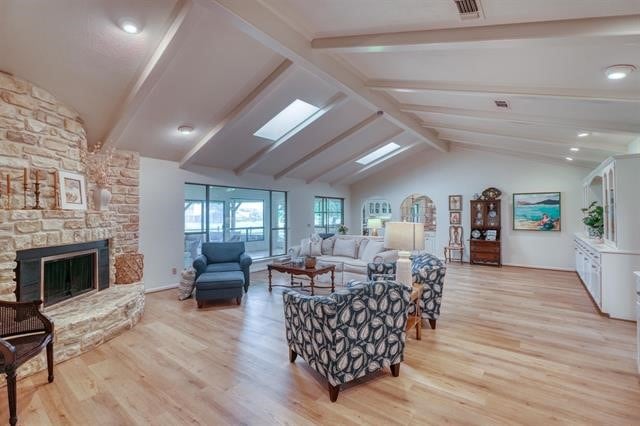 living room featuring a stone fireplace, lofted ceiling with skylight, and light hardwood / wood-style floors