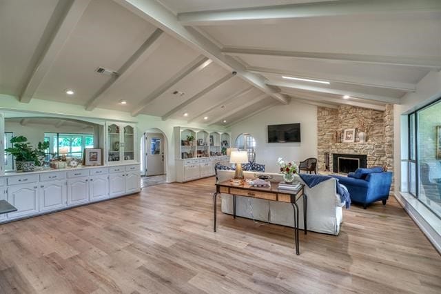 living room featuring light hardwood / wood-style flooring, a fireplace, and vaulted ceiling with beams