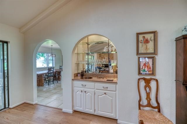 bar with beamed ceiling, sink, white cabinetry, and light wood-type flooring