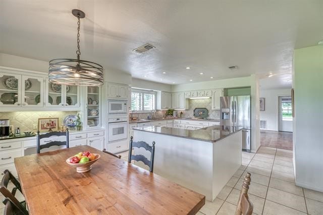 kitchen featuring white appliances, light tile patterned floors, white cabinets, a center island, and decorative backsplash