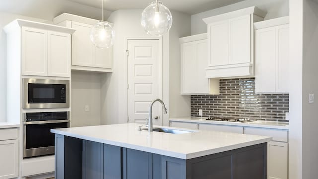 kitchen with appliances with stainless steel finishes, sink, an island with sink, decorative light fixtures, and white cabinets