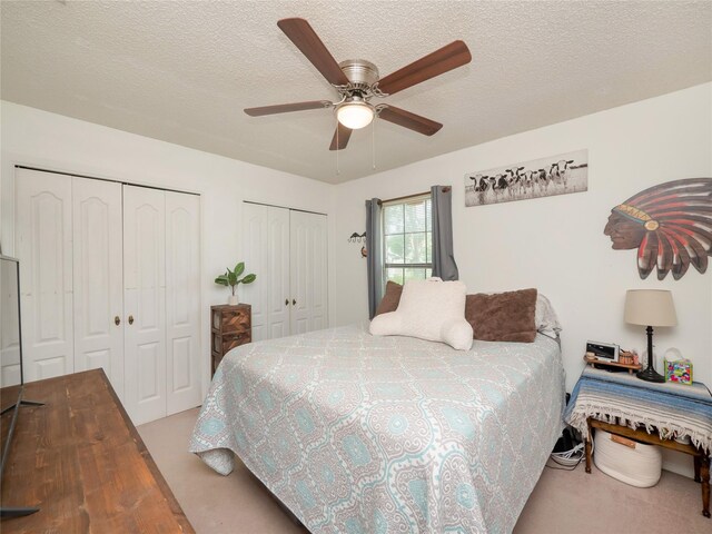 carpeted bedroom with multiple closets, a textured ceiling, and ceiling fan