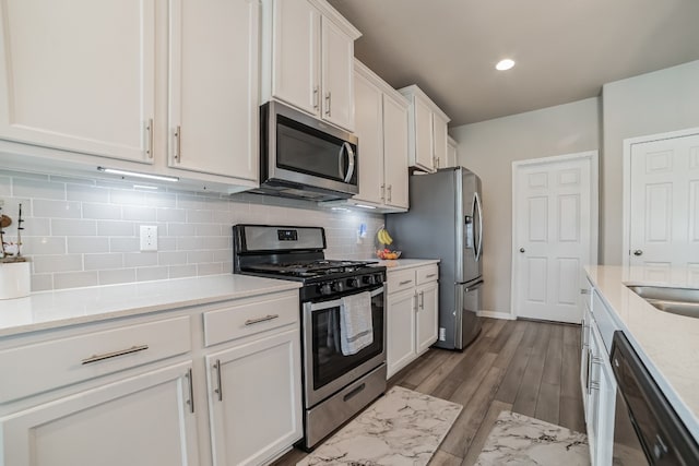 kitchen featuring white cabinetry, hardwood / wood-style flooring, stainless steel appliances, decorative backsplash, and light stone countertops