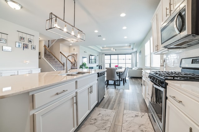 kitchen with light hardwood / wood-style flooring, white cabinets, light stone counters, a tray ceiling, and stainless steel appliances