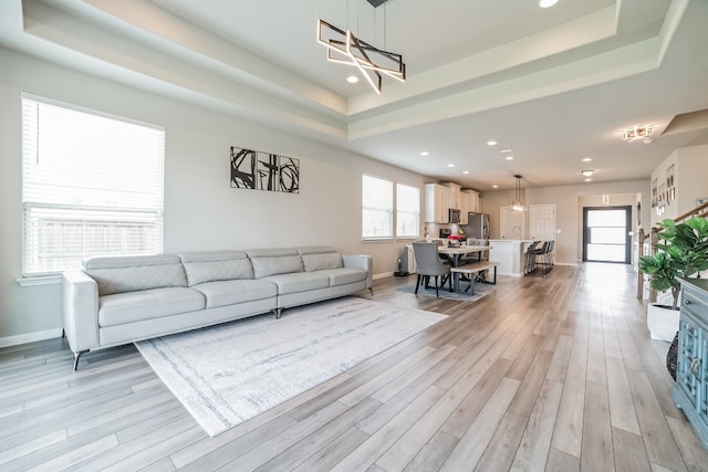 living room with sink, a tray ceiling, and light hardwood / wood-style floors