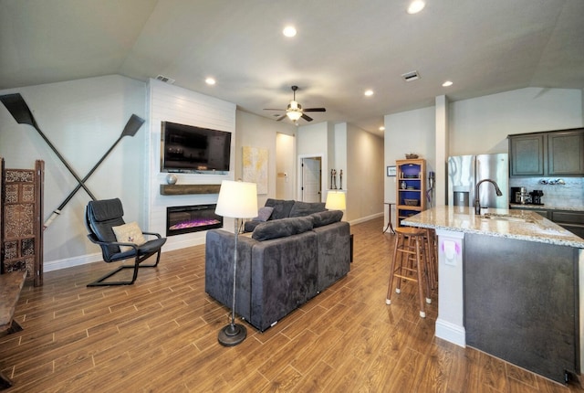 living room with lofted ceiling, a fireplace, sink, and light hardwood / wood-style flooring