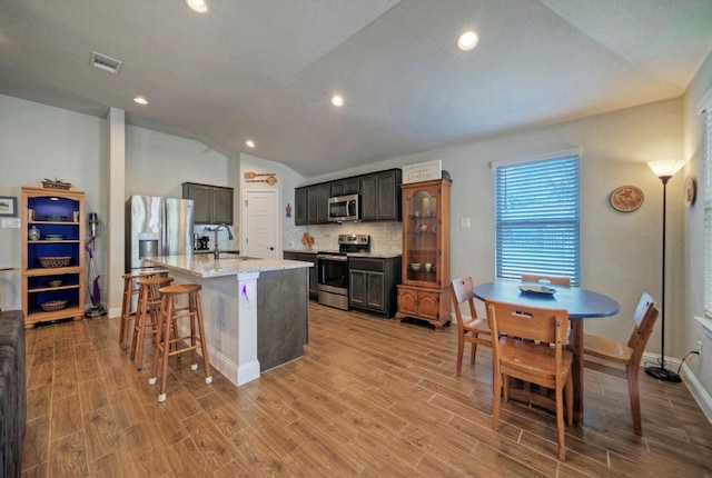 21707 Crystal Way, Lago Vista, TX 78645 - kitchen with appliances with stainless steel finishes, a sink, decorative backsplash, light wood-style flooring, and a center island with sink