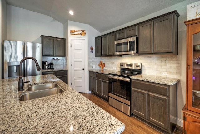 kitchen with dark brown cabinetry, sink, light stone counters, stainless steel appliances, and hardwood / wood-style floors