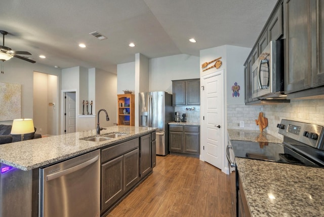 kitchen featuring decorative backsplash, light stone counters, stainless steel appliances, a kitchen island with sink, and sink